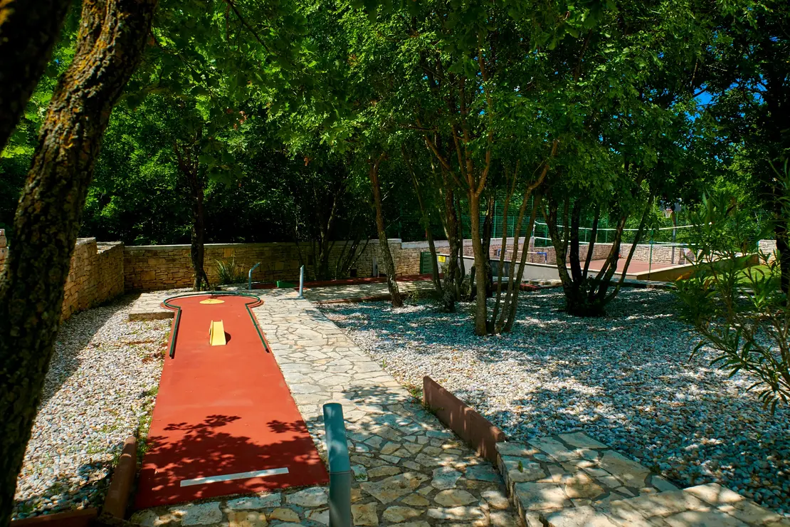 Einzelne rote Minigolfbahn mit Hindernissen im schattigen Garten der Villa Štokovci